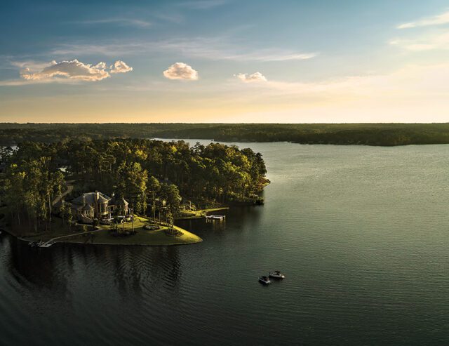 Large house on a wooded peninsula jutting into a lake, with two boats on the water.