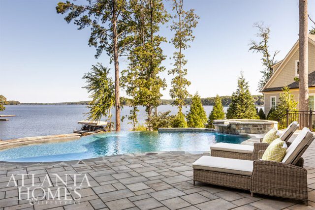 Infinity pool and hot tub overlooking a lake with trees and a house.
