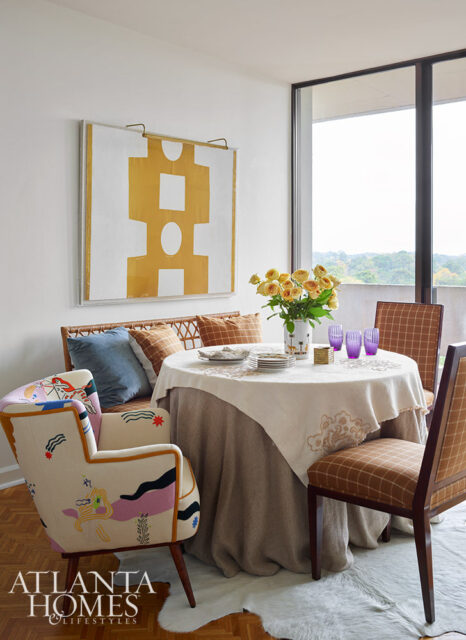 Dining area with round table, upholstered chairs, wicker bench, and abstract art.