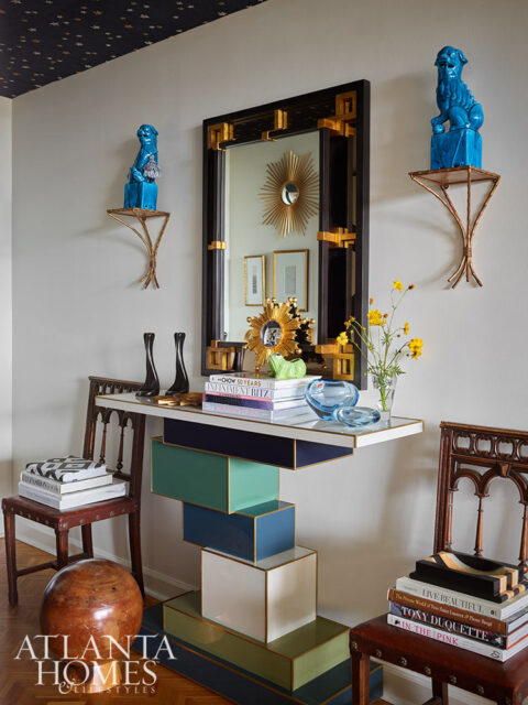 Console table with stacked colorful drawers, mirror, blue foo dogs on shelves, and books.
