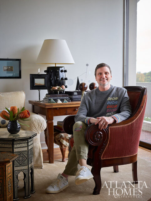 Man in gray sweater with 'DIOR' text sits in ornate red chair.