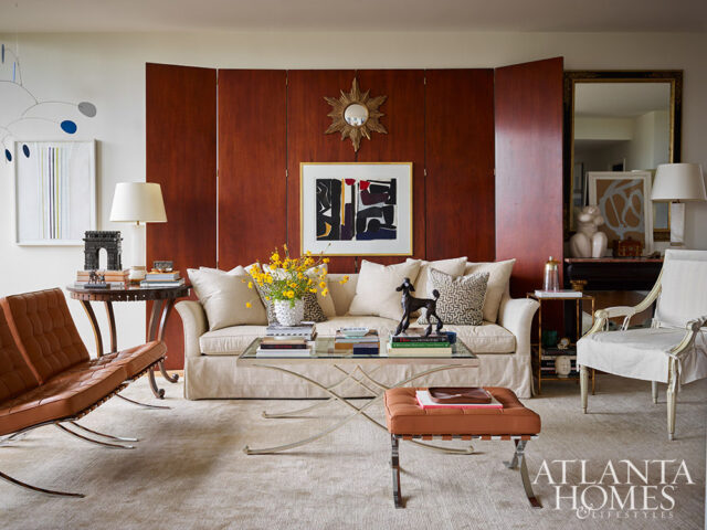 Living room with neutral sofa, leather chairs, wood paneling, and abstract art.