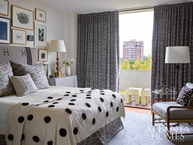 Bedroom with grey patterned curtains, bed with polka dot throw, and framed art on wall.