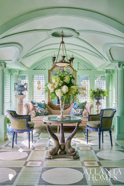 Light green sunroom with arched ceiling, sofa, chairs, and ornate table with dolphin legs.
