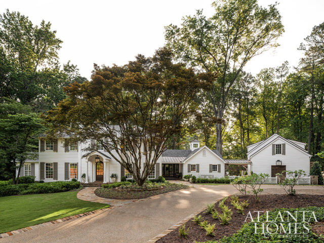 White house with gray shutters and a large tree in the front yard.