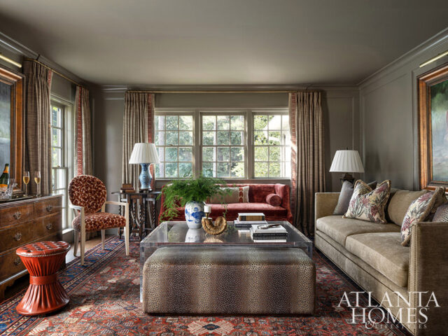 Living room with taupe sofa, red settee, animal print ottoman, and ornate rug.