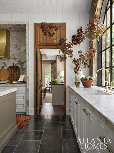Kitchen with marble countertops, white cabinets, brass hardware, and stone floor.