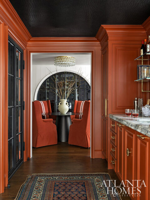 Orange paneled room with black textured ceiling and view into dining area with orange chairs