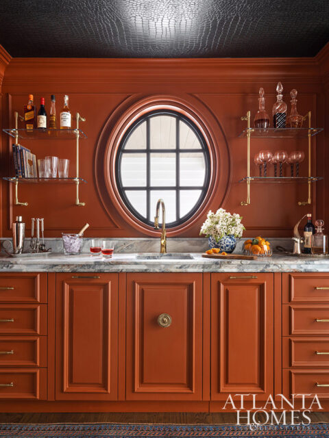 Orange bar with marble countertop, round window, and glass shelves with bottles and glassware.