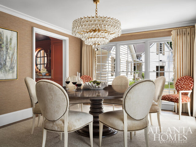 Dining room with round table, upholstered chairs, crystal chandelier, and view of white house
