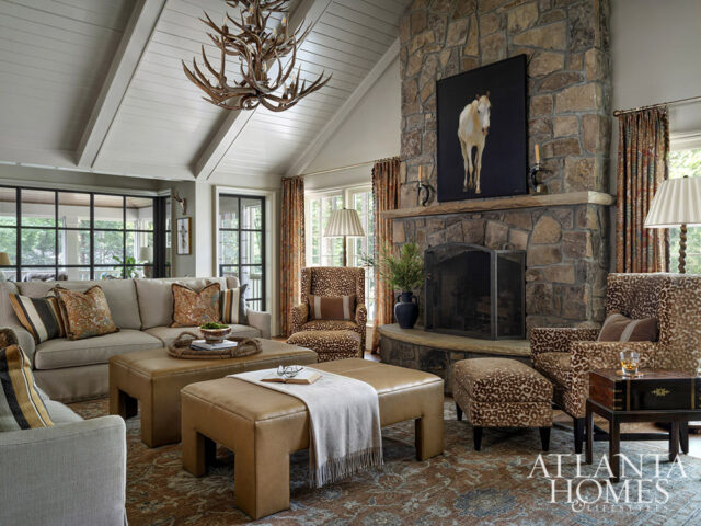 Living room with stone fireplace, antler chandelier, and leopard print chairs.
