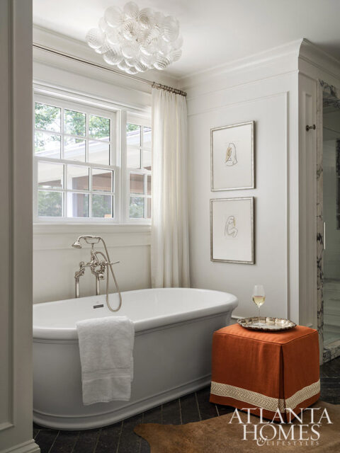 White freestanding bathtub with chrome fixtures and a white towel. Orange ottoman with decorative