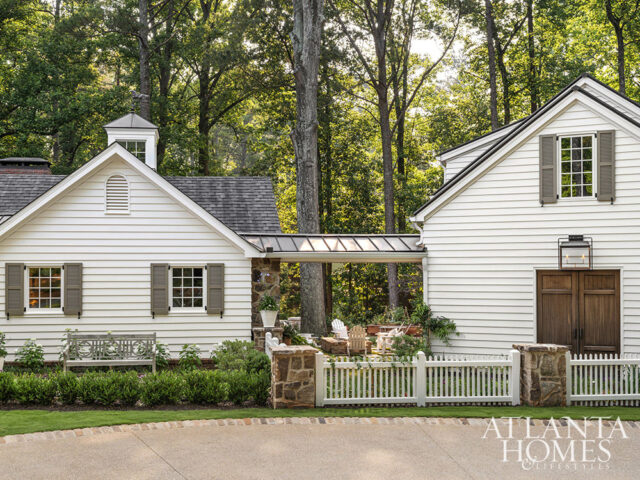 White clapboard house with stone accents, dark wood garage doors, and white picket fence.