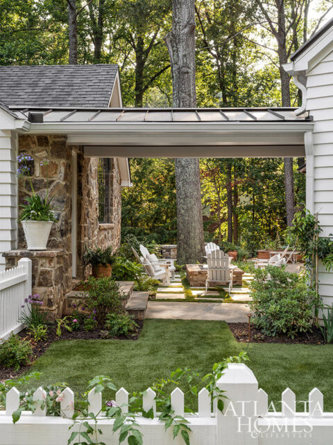 Stone house with white picket fence and Adirondack chairs around a fire pit