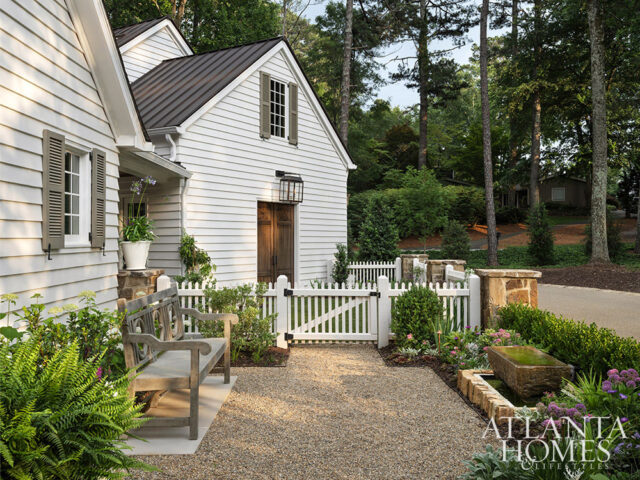 White clapboard house with dark metal roof, wooden doors, and picket fence.