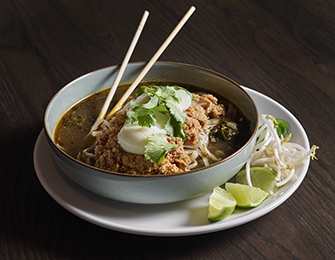 Bowl of noodles with meat, egg, cilantro, lime, and bean sprouts, with chopsticks