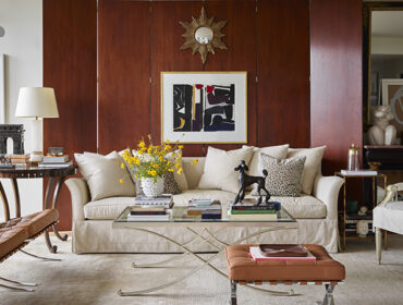 Living room with wood paneled walls, neutral sofa, leather Barcelona chair, and glass coffee table.