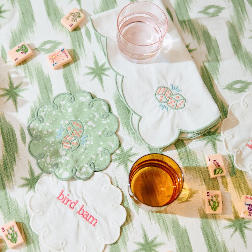 Mahjong tiles and embroidered coasters on a green and white striped tablecloth.