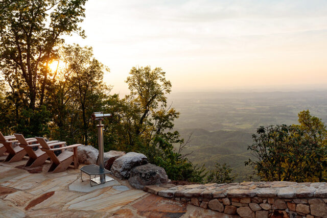 Stone patio with Adirondack chairs and telescope overlooking a valley at sunset