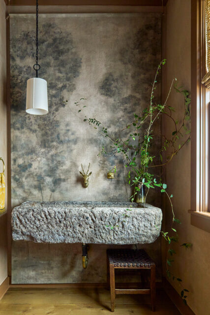 Powder room with stone trough sink, deer head wall mount, and forest mural wallpaper.