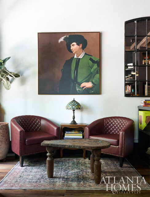 Living room with two burgundy leather chairs, a vintage coffee table, and a portrait painting.