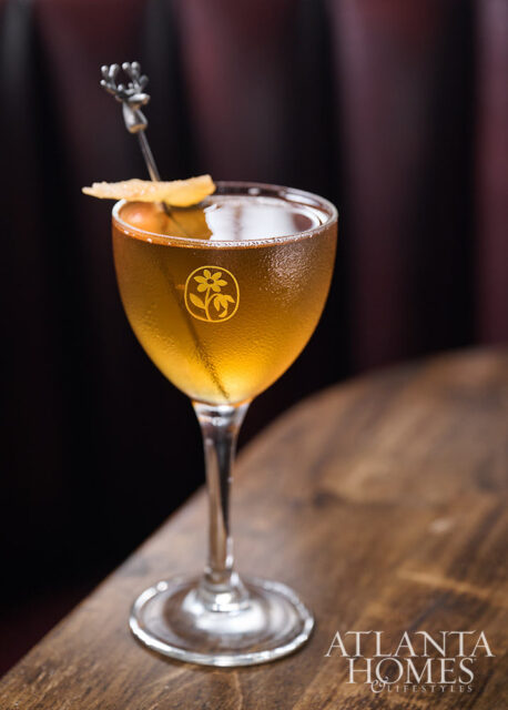 Cocktail with a flower logo etched on the glass and a deer-shaped pick.