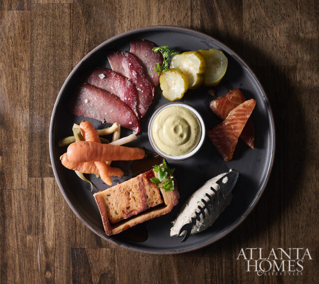 Charcuterie board with sliced meats, pickles, carrots, pâté, and mustard dip.