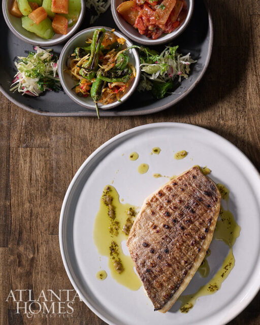 Grilled fish fillet with herbs and olive oil on a white plate, with a side of appetizers.