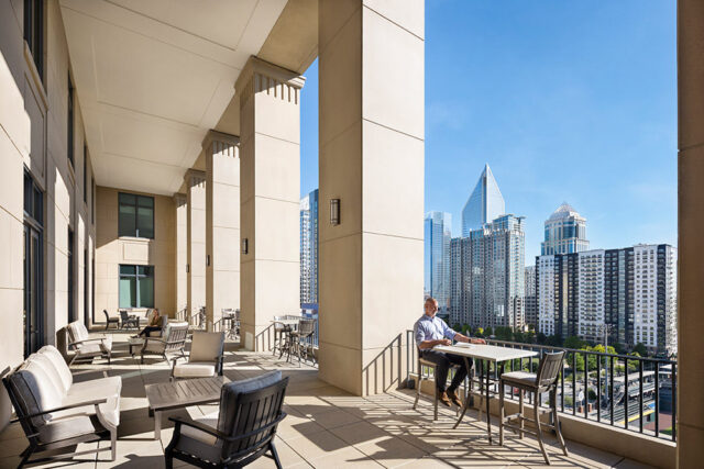 Balcony with seating and city skyline view. Man sits at table.