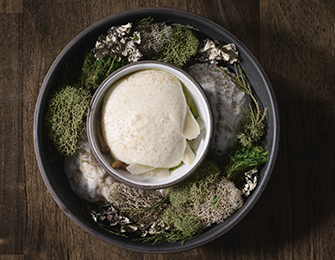 Creamy mousse served in a bowl surrounded by moss and decorative elements