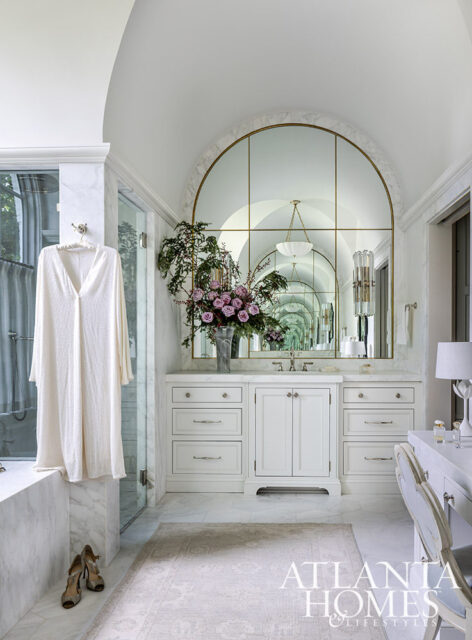 White marble bathroom with arched mirror, vanity, and bathtub.