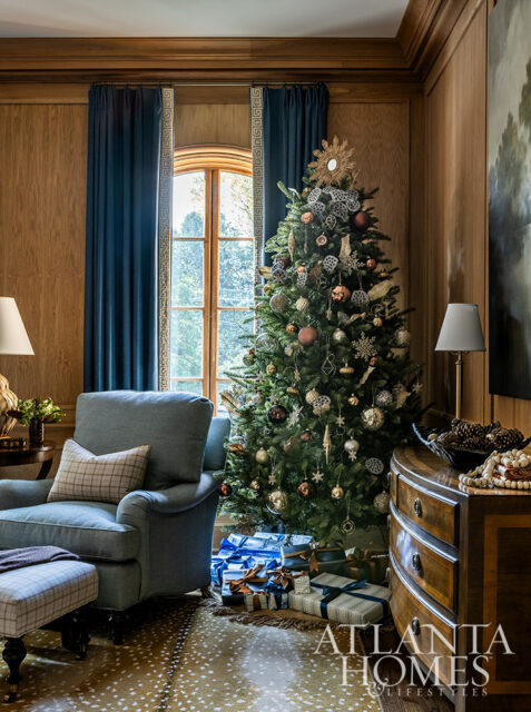 Living room with Christmas tree, blue armchair, and wood paneled walls.