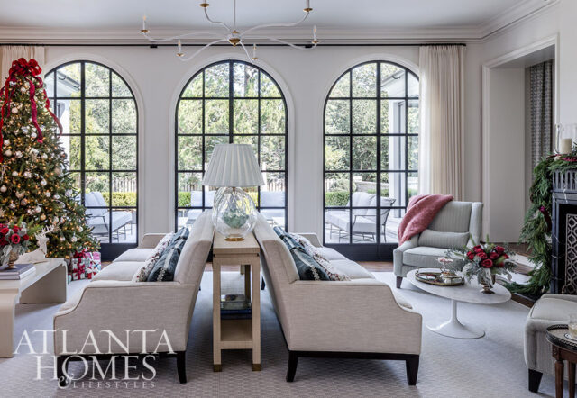 Living room with arched windows, Christmas tree, neutral sofas, and a pink throw on a chair.
