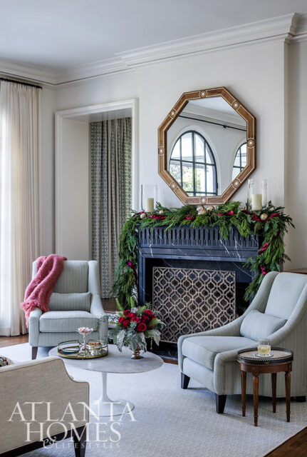 Living room with light blue armchairs, marble coffee table, and fireplace decorated for Christmas.