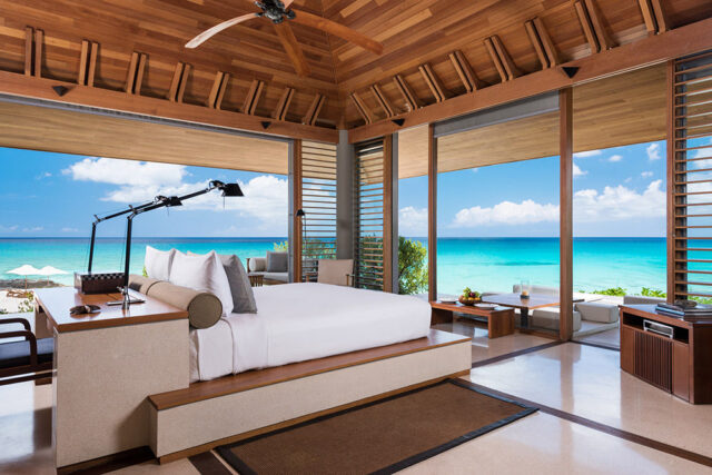Bedroom with white bedding, wooden ceiling, and ocean view.