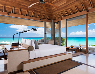 Bedroom with white bed and wooden ceiling, opening to ocean view