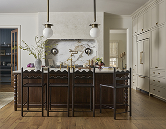 Kitchen island with dark wood base, marble backsplash, and brass faucet. Cream cabinetry and