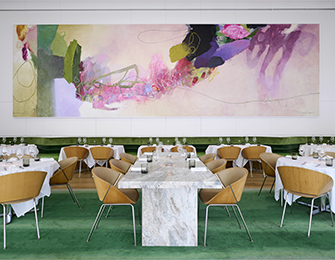 Dining room with green carpet, marble table, and abstract art above banquette seating.