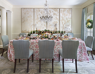 Dining room with a table set for a meal, floral tablecloth, light blue chairs, and three framed
