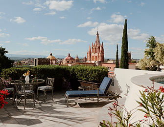 Terrace with seating overlooking a city with a prominent church spire and lush greenery