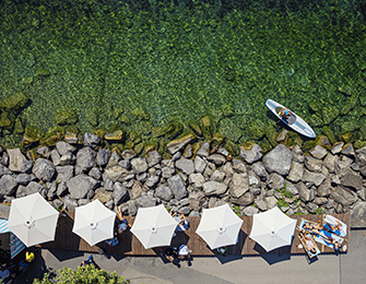 Aerial view of a rocky shoreline with clear green water, lounge chairs under umbrellas, and a