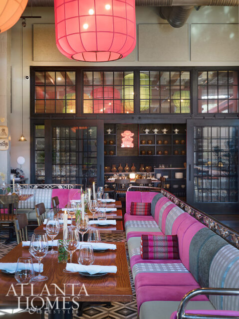 Restaurant dining room with pink banquette seating, wooden tables, and large pink lanterns overhead.