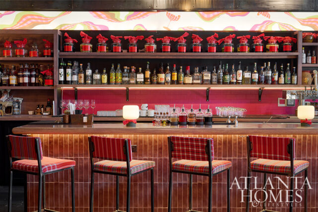 Bar with red plaid stools, pink tile backsplash, and shelves stocked with liquor bottles.