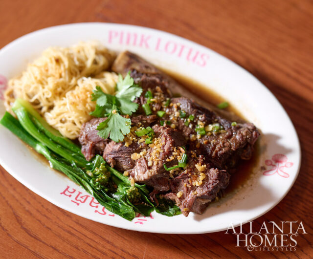 Braised beef with noodles and greens on a plate with "Pink Lotus" text.