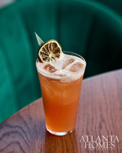 Pink cocktail with ice, garnished with dried lime and a leaf, on a wooden table.