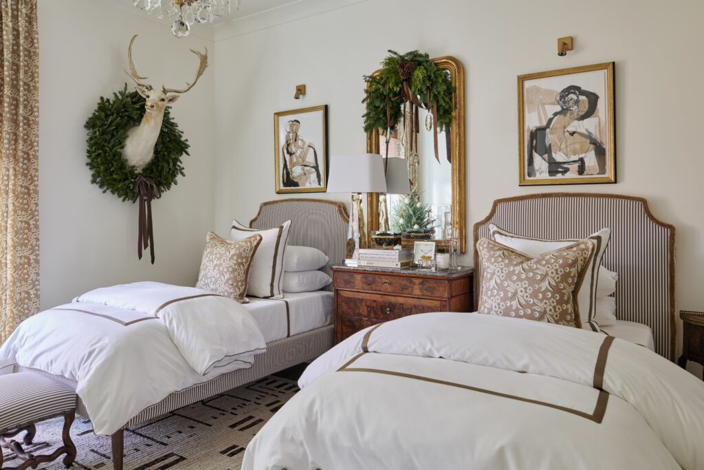 Bedroom with two twin beds, white bedding, striped headboards, and mounted deer head with wreath.