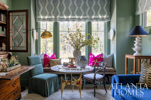 Green room with bay window, round table, blue sofa, and patterned pillows.