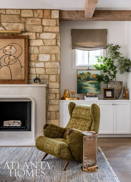 Living room with stone fireplace, green patterned armchair, and built-in white cabinets.