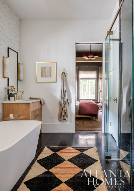 White bathroom with freestanding tub, wood vanity, black marble floor, and diamond-patterned rug.