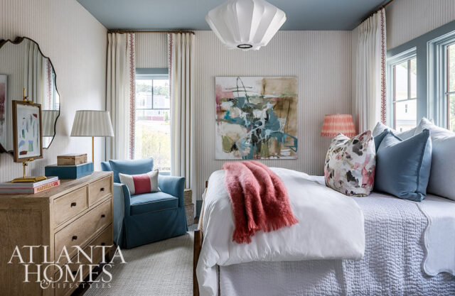 Bedroom with blue armchair, abstract art, and striped wallpaper.